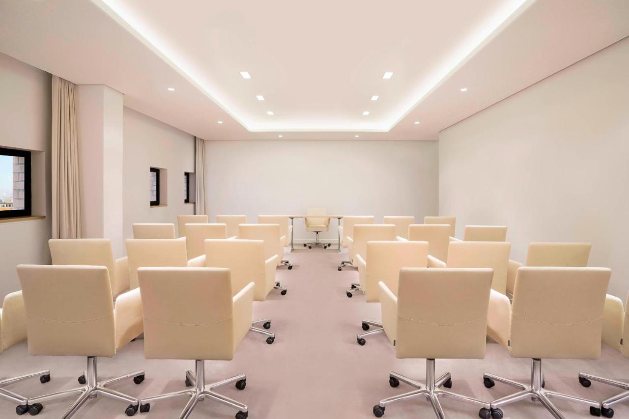 The Westin Hamburg Elbphilharmonie Hotel Exterior photo The photo shows a modern conference room. There are several light-colored, wheeled chairs arranged in rows facing a central area where a glass table is located. The room has soft lighting from recessed ceiling lights, and the walls are mostly white, 