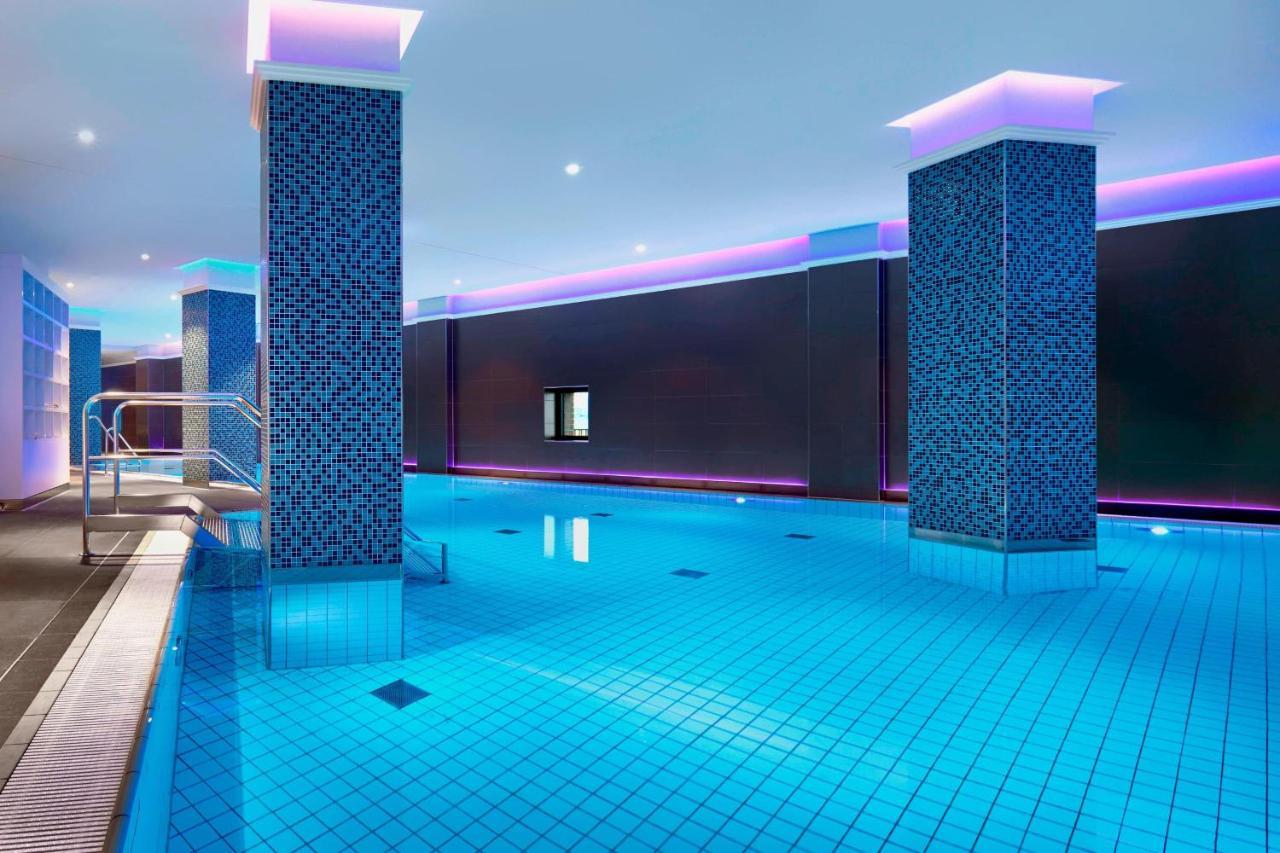 The Westin Hamburg Elbphilharmonie Hotel Exterior photo The image shows a swimming pool area that features a modern, upscale design. The pool has bright blue tiles reflecting the water, creating a vibrant atmosphere. There are two columns dressed in a similar blue tile pattern, and the walls are adorned w