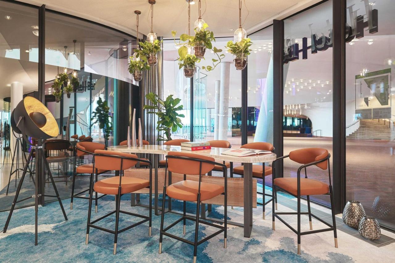 The Westin Hamburg Elbphilharmonie Hotel Exterior photo The image depicts a modern indoor seating area designed for gatherings or meetings. There is a long table surrounded by several bar-style chairs with brown upholstery. Above the table, there are hanging plants that add a touch of greenery to the spac
