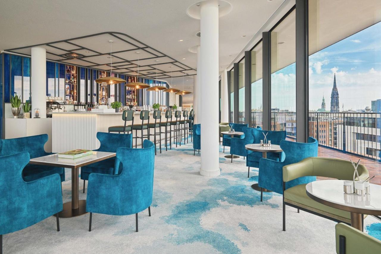 The Westin Hamburg Elbphilharmonie Hotel Exterior photo The image shows a stylish and modern restaurant interior. There are several tables with blue and green chairs, creating a cozy atmosphere. The flooring features a light carpet with abstract patterns. Large windows provide plenty of natural light and 