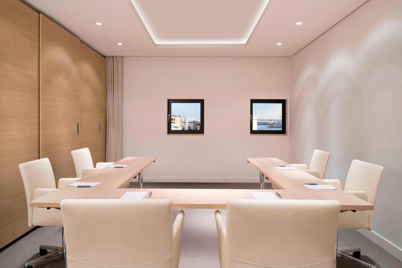 The Westin Hamburg Elbphilharmonie Hotel Exterior photo The photo shows a modern conference room. It features a long, rectangular table made of light-colored wood, surrounded by several cream-colored chairs. The walls are painted in a light shade, and there are two framed windows on one wall that provide 