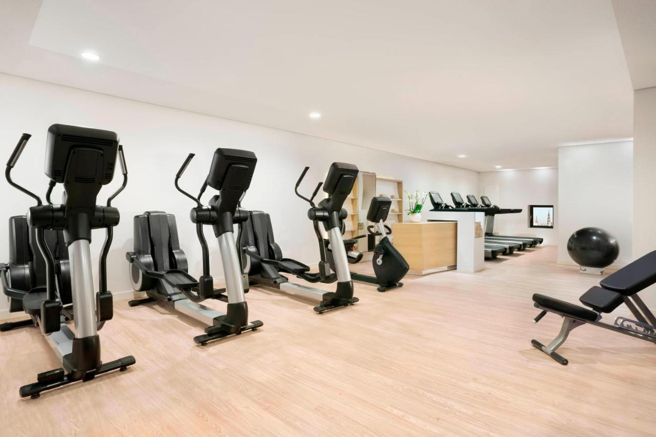 The Westin Hamburg Elbphilharmonie Hotel Exterior photo The photo shows a fitness room with several pieces of exercise equipment. On the left side, there are multiple elliptical machines arranged in a row. In the center, there is a stationary bike. A workout bench is positioned nearby, and a large exercis