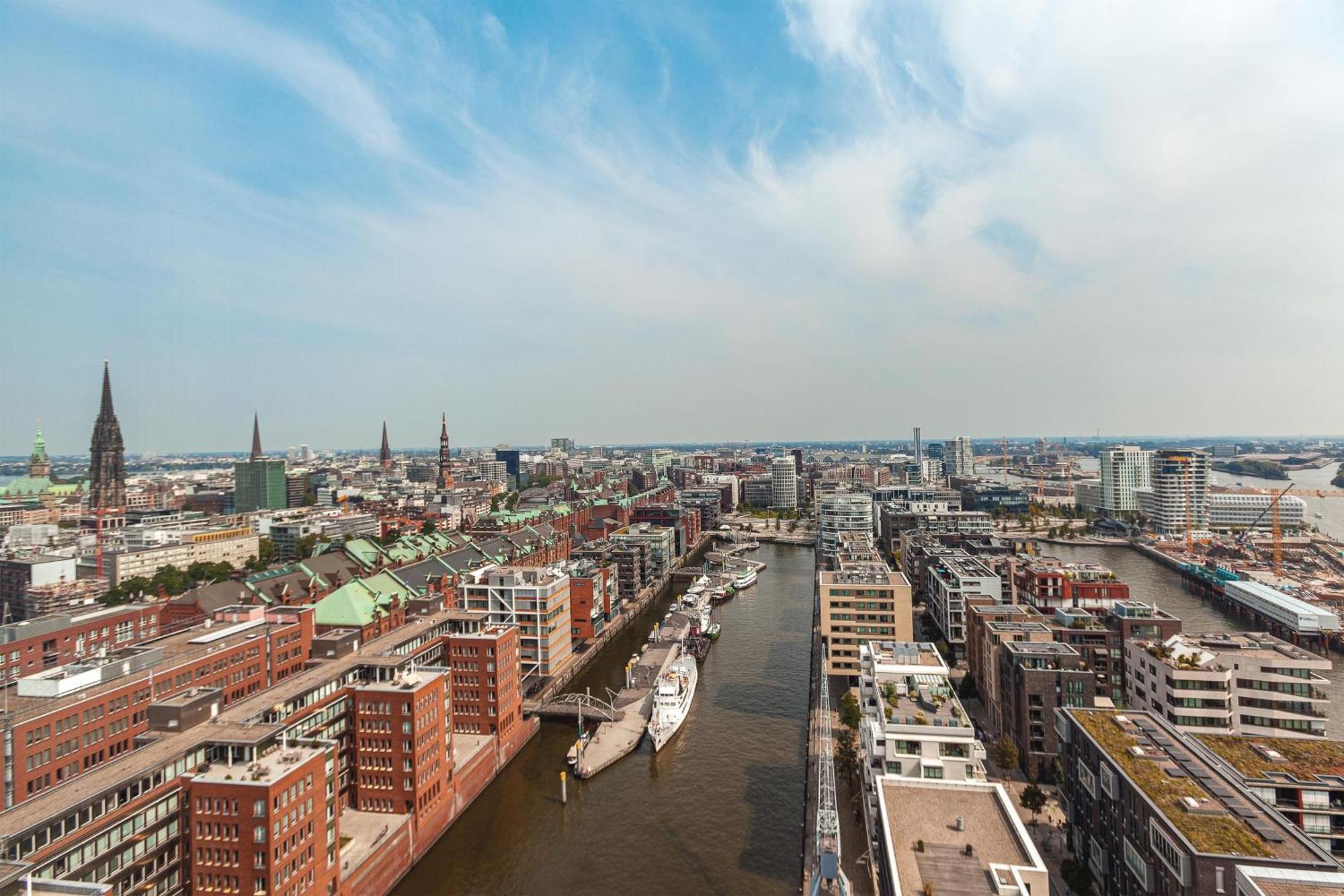 The Westin Hamburg Elbphilharmonie Hotel Exterior photo The photo shows an aerial view of a cityscape with a prominent waterfront area. There are modern and historic buildings lining both sides of a river or canal, suggesting an urban environment. The architecture appears diverse, with a mix of contempora